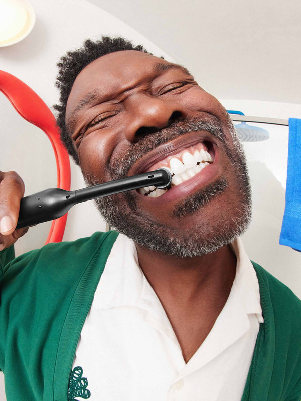 A man smiles while brushing her teeth with quip 360 oscillating electric toothbrush