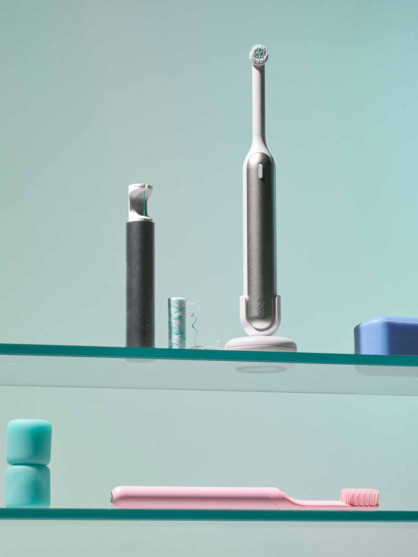 quip 360 oscillating toothbrush sits on a medicine cabinet shelf, along with a quip flosser