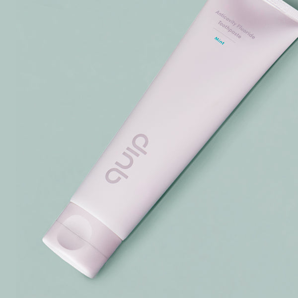 A tube of quip anticavity fluoride toothpaste in flavor mint against a green background