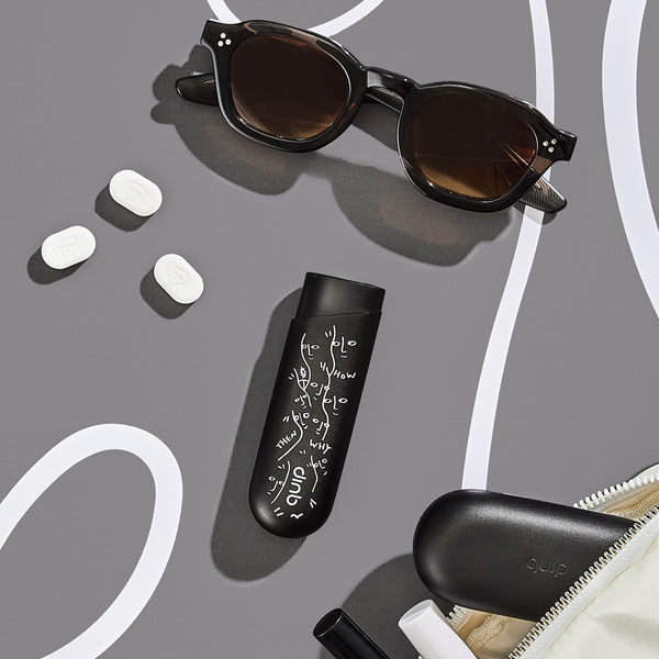 The quip gum dispenser- Shantell Martin Special Edition on the table with sunglasses and a make up pouch