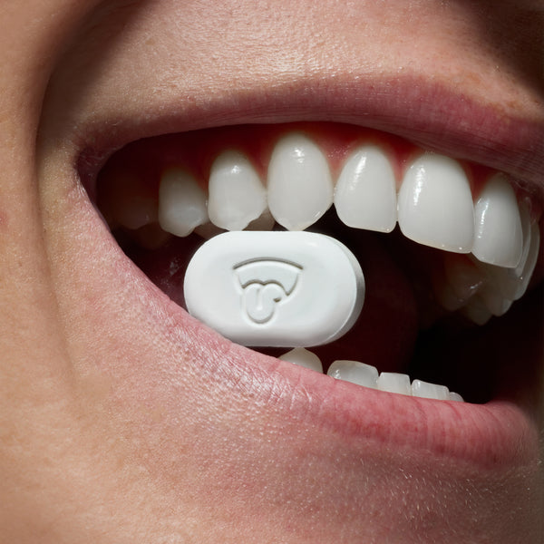 A model smiles while holding a piece of quip mint between her teeth