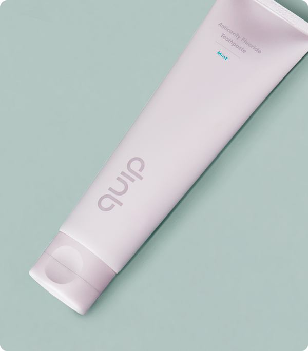 A tube of quip anticavity fluoride toothpaste in flavor mint against a green background