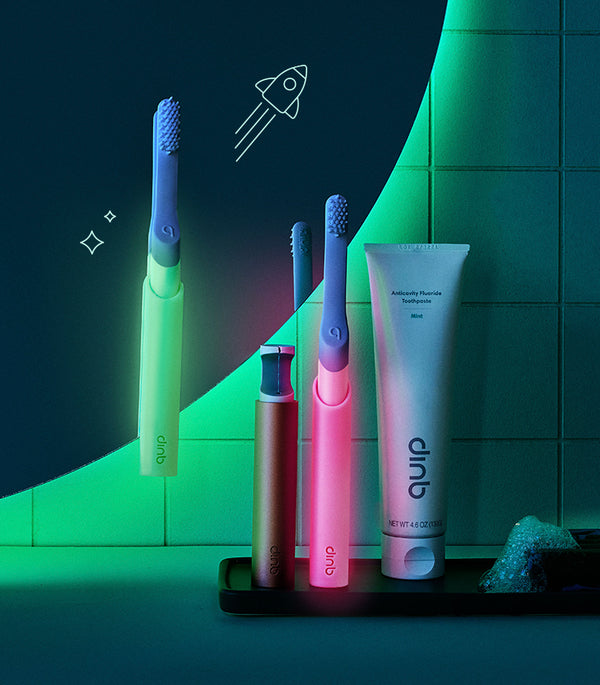 quip's glow in the dark adult toothbrushes in green and in pink on a bathroom counter, with the lights off and they are glowing. 